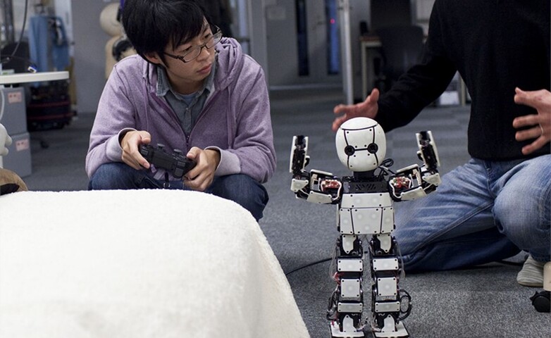 Ein junger Student programmiert mit einem Gamecontroller einen humanoiden Roboter in einer Lehrveranstaltung eines technischen Studiengangs.