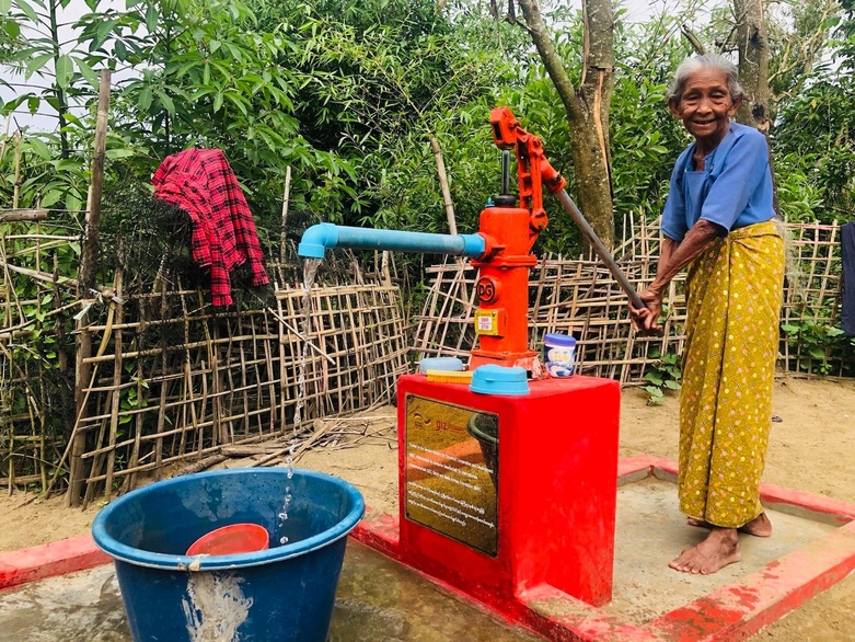 Eine Frau in Myanmar pumpt fröhlich sauberes Wasser.