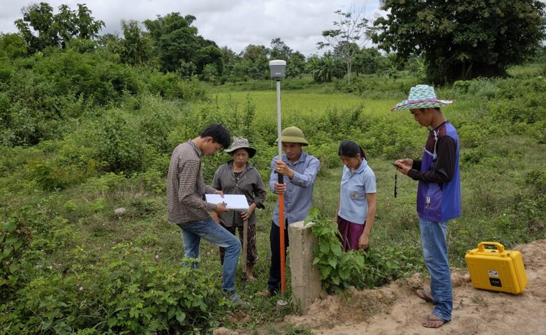 Eine fünfköpfige Gruppe, umgeben von üppiger Vegetation, verwendet Echtzeitkinematik (RTK)-Ausrüstung zur Landvermessung und systematischen Landregistrierung.