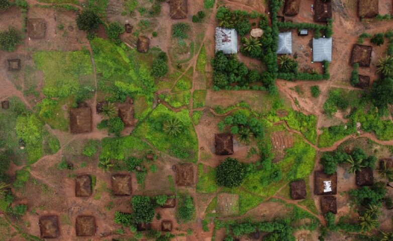 Aus der Vogelperspektive: Dorf mit kleinen, verstreut stehenden Häusern und intensiv grüner Vegetation in der Regenzeit.