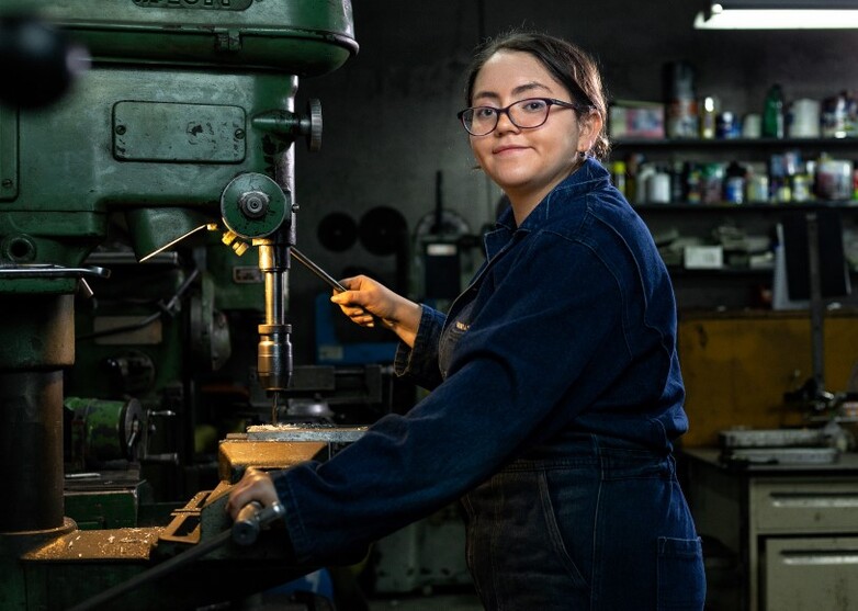 Eine auszubildende Industriemechanikerin bedient eine Arbeitsmaschine in einer Werkstatt. 