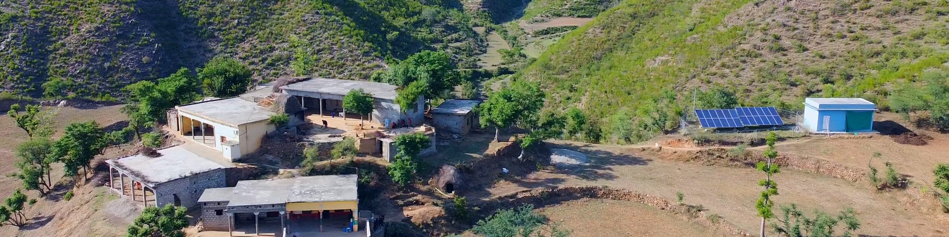 Ein abgelegenes Dorf in einer hügeligen Region mit einer Ansammlung kleiner Gebäude im Grünen und einer Solaranlage auf der rechten Seite.