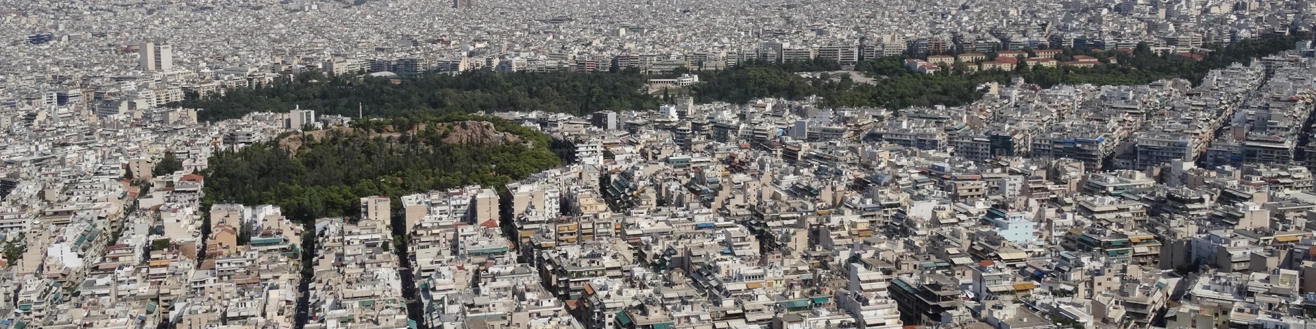 Eine Luftaufnahme von Athen auf der ein Stadtpark eine grüne Insel zwischen vielen Gebäuden bildet.