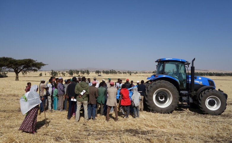 Eine Gruppe von Landwirt*innen und ein Traktor stehen auf einem Stoppelfeld.