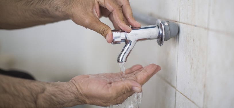 Nahaufnahme von den Händen eines Mannes, über die Wasser aus einem Wasserhahn läuft.