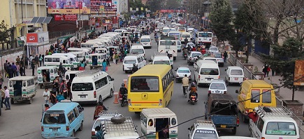 Eine belebte Straße mit zahlreichen Fahrzeugen und Fußgängern, die in verschiedene Richtungen unterwegs sind.