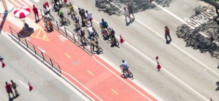 Blick von oben auf eine Straße mit rot markiertem Radweg, auf dem zahlreiche Menschen Fahrrad fahren.