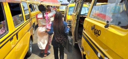 Zwei Frauen gehen zwischen gelben Taxibussen in der Großstadt Lagos (Nigeria) entlang.