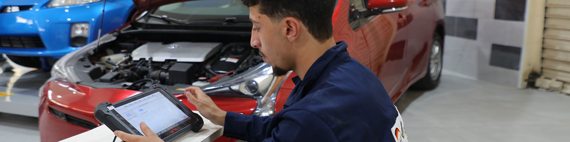 A young apprentice checks the battery voltage for hybrid cars on a tablet in a car workshop.