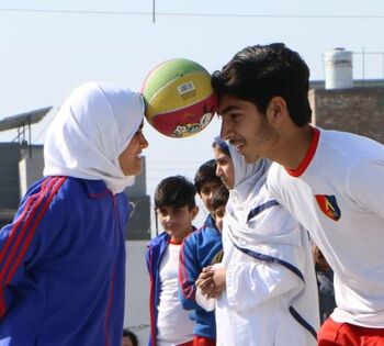 A young man and a woman play with a soccer ball.