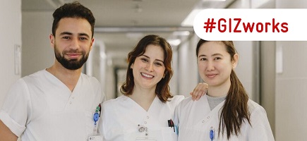 Three qualified nurses stand in a hospital corridor smiling in the camera.