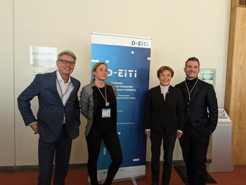 Four members of the D-EITI multi-stakeholder group stand together in front of a banner.