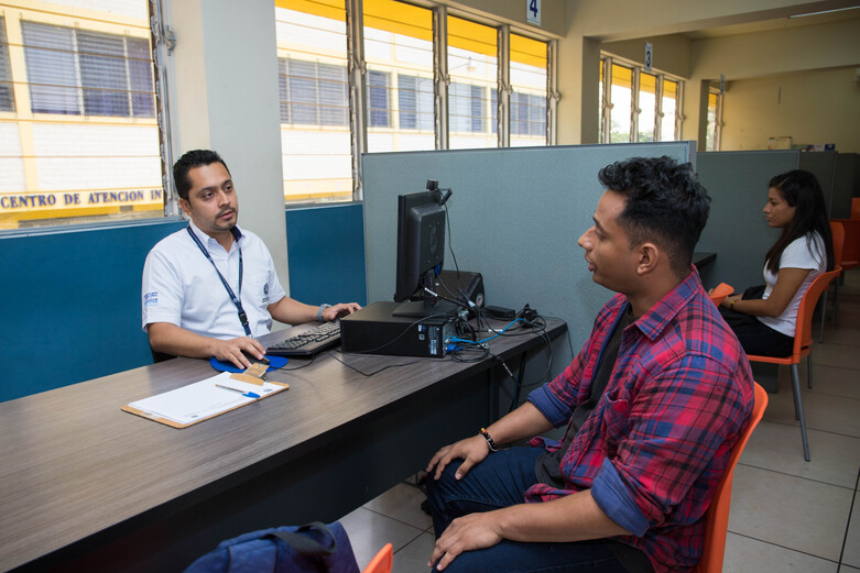 A man sitting with a staff member at an immigration office.