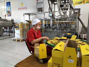 A person with cap and protective mask in a factory room is packing yellow parcels.