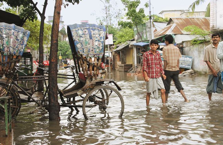 People wade through in a flooded street in Bangladesh. Two of them look at the camera. 