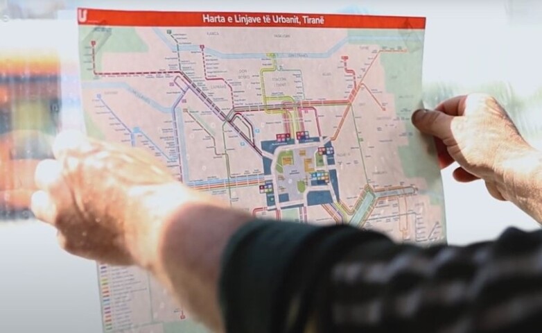 Hands holding a printed bus route map inside a bus in Tirana, Albania.