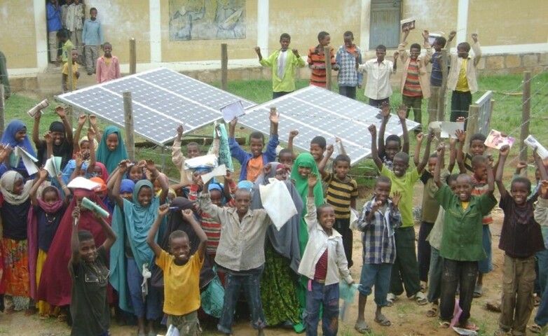 A group of children in Ethiopia celebrating in front of solar panels.