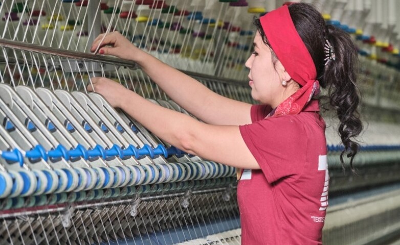 A woman operating a large weaving machine, processing cotton yarn into fabric in a textile factory.