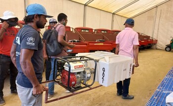 Workers in a large tent carry a piece of fire extinguishing equipment provided to the Refugee Relief and Repatriation Commis-sioner (RRRC).