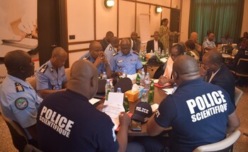 A group of police officers and individuals dressed in civilian clothes engage in a lively discussion during a workshop, focusing on documents on a table in a conference room.