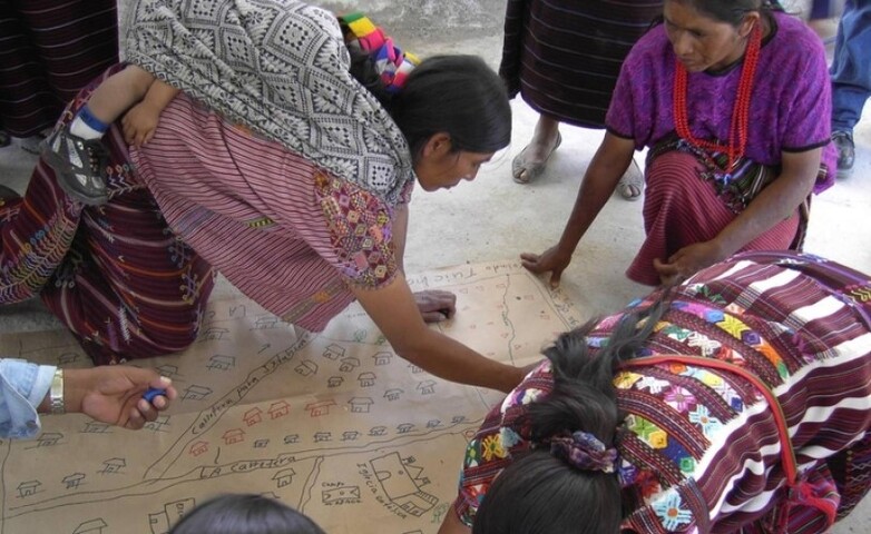 Mujeres indígenas guatemaltecas examinando un mapa comunitario dibujado a mano.