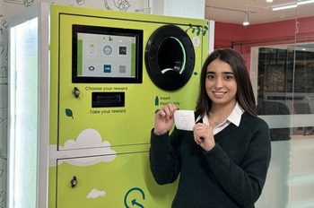 Business founder Prusha Awat Mohamat stands in front of her prototype of a reverse vending machine and holds a voucher in her hand.