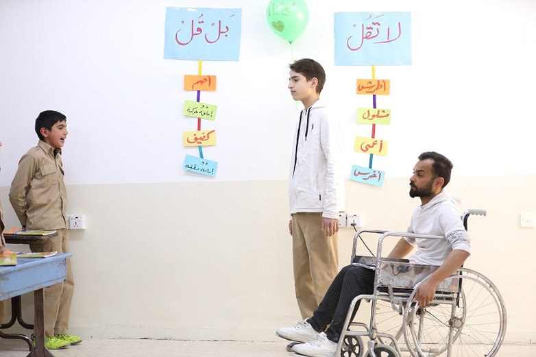 School students stand in a classroom during a training on disability inclusive language. One man is a wheelchair user. 