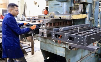 A man in a blue work jacket operates a large industrial machine in a workshop.