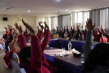 Women sit together at a table and raise their hands.