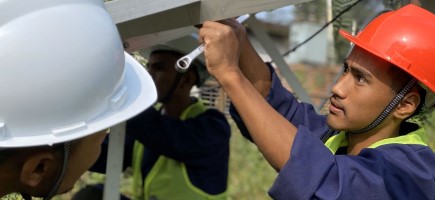 A man wearing a red safety helmet and holding a spanner examines a metal structure.