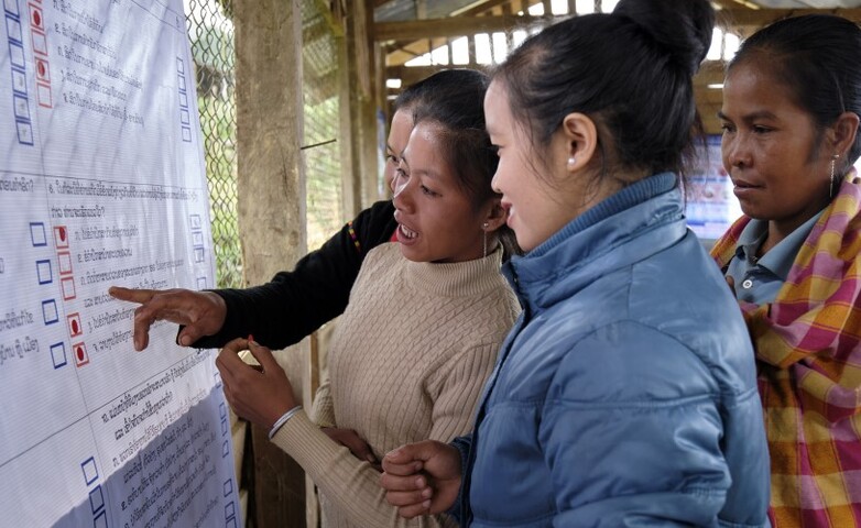 Three women are examining and discussing a large informational poster about land use rights and conflict resolution.