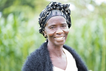 A woman with her hair tied up in a headscarf and wearing a black cardigan smiles into the camera.