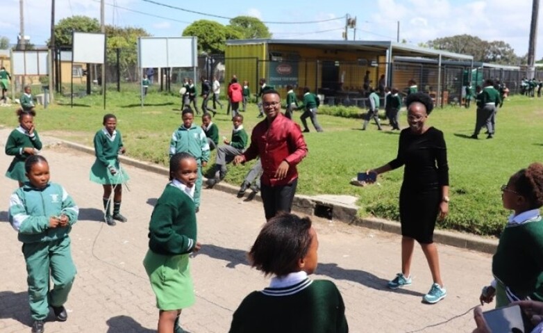 Schoolchildren in green uniforms play and interact with two adults in a playground.