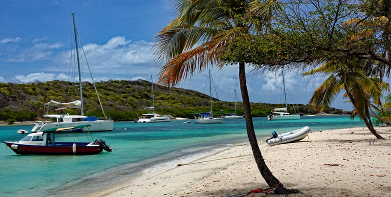 A boat lies on the beach near palm trees, surrounded by sandy shores and clear skies.