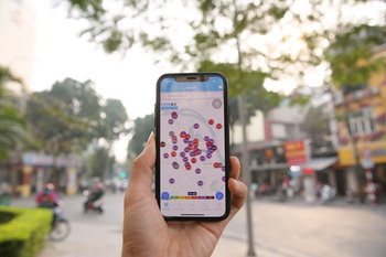 A hand holds a smartphone. The app displays air data from Hanoi.