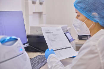 A lab technician compares data on the computer with a paper document.