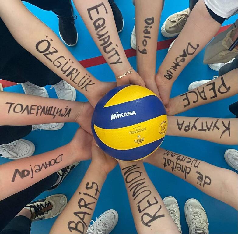 A group of young people hold a volleyball together.