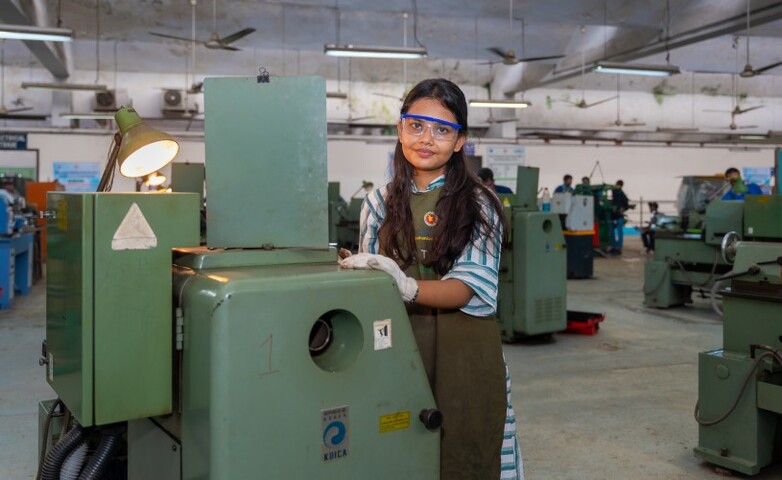 A woman wearing blue protective glasses stands behind a machine. 