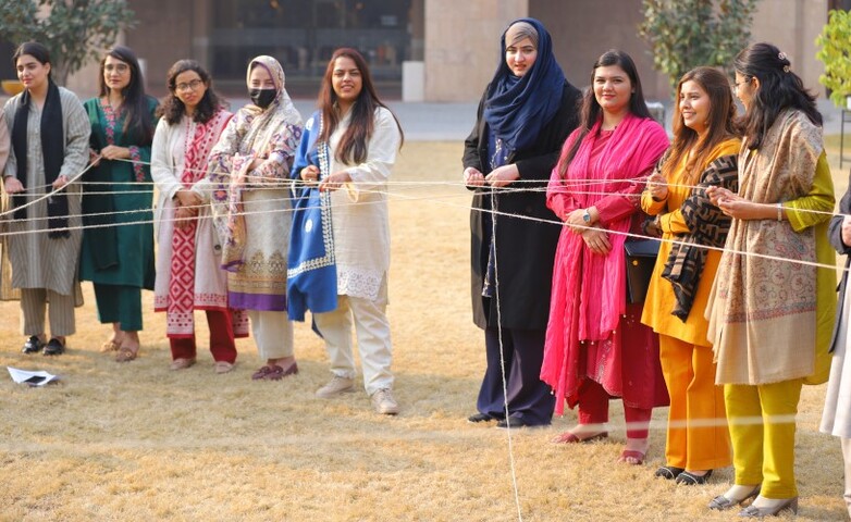 A group of young women participate in an empowering team-building activity outdoors in Islamabad.