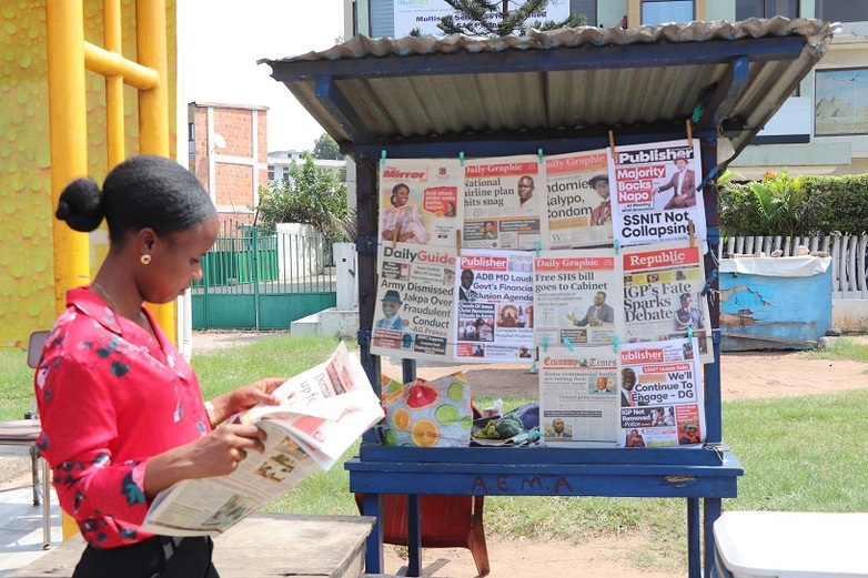 A woman reading a newspaper at a newsstand.