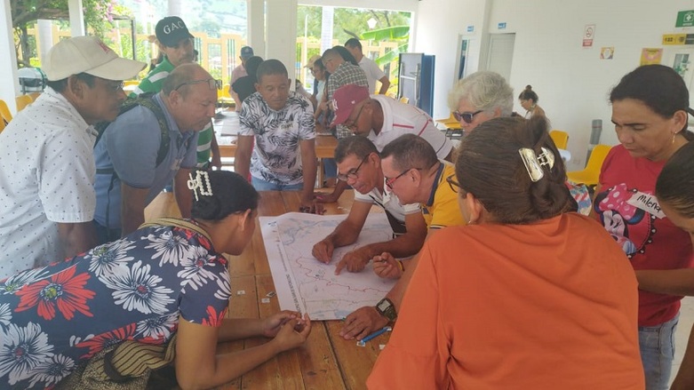 Several people standing around a map. A man is marking a point on the map.