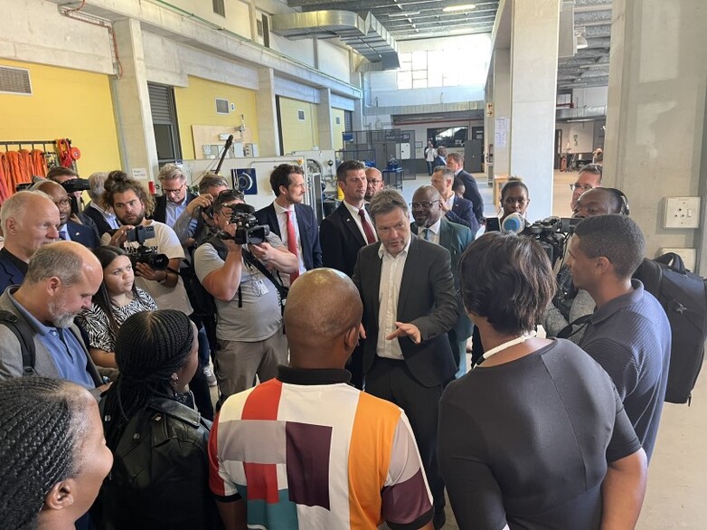 A group of people, some with cameras and microphones, stand around Minister for Economic Affairs Habeck on his visit to a renewable energy training centre in Cape Town.