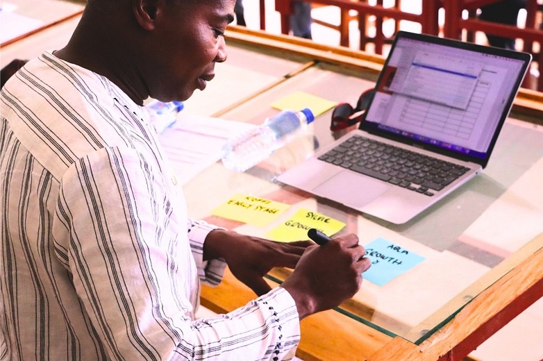 A man at a laptop is writing notes on slips of paper.