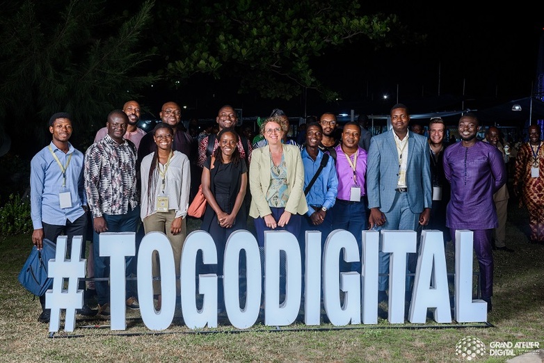 A group of people are standing behind large letters spelling Togodigital