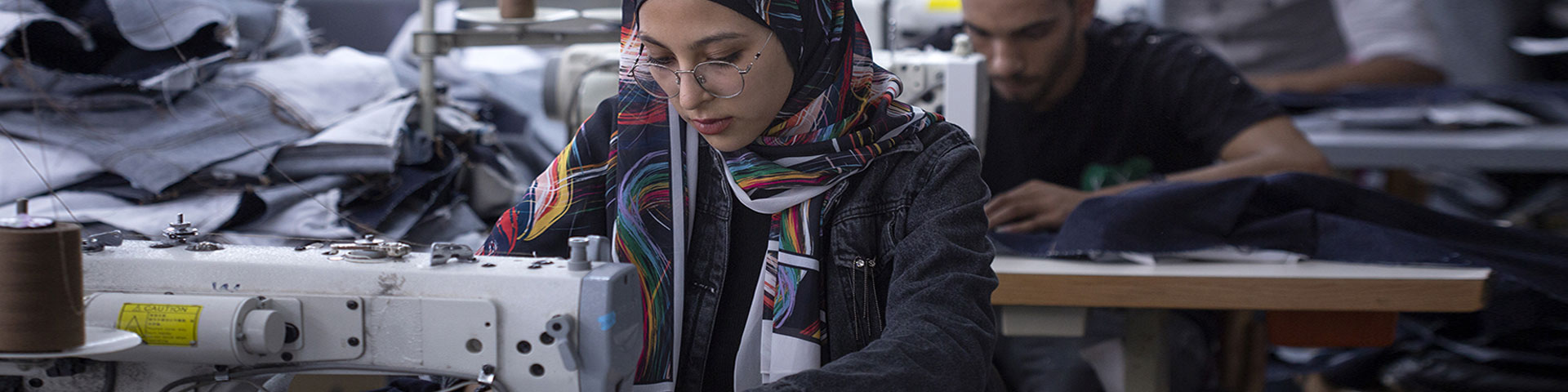 A young woman working at a sewing machine in a factory.