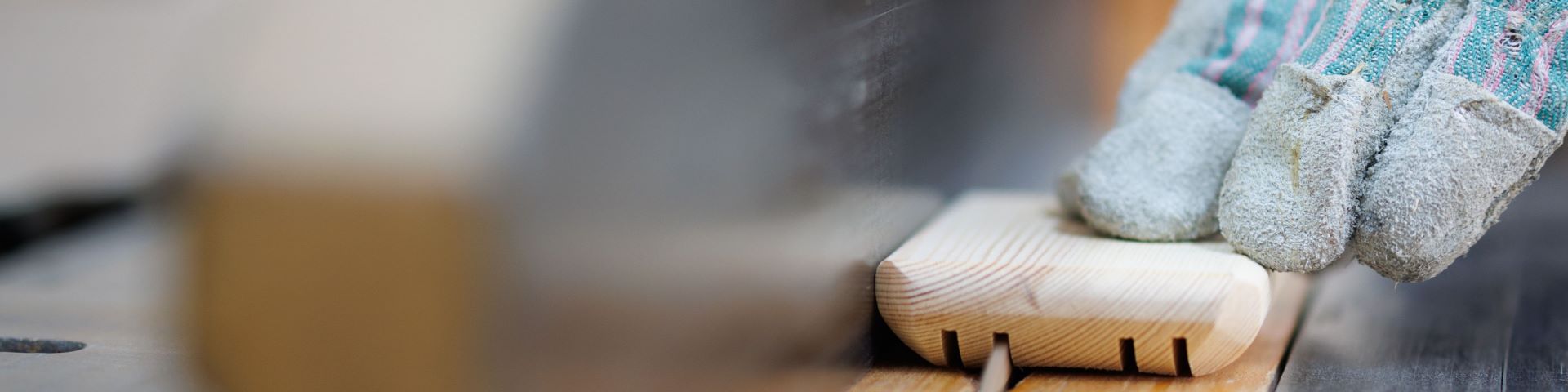 A hand wearing a protective glove guiding a piece of wood along a saw bench.