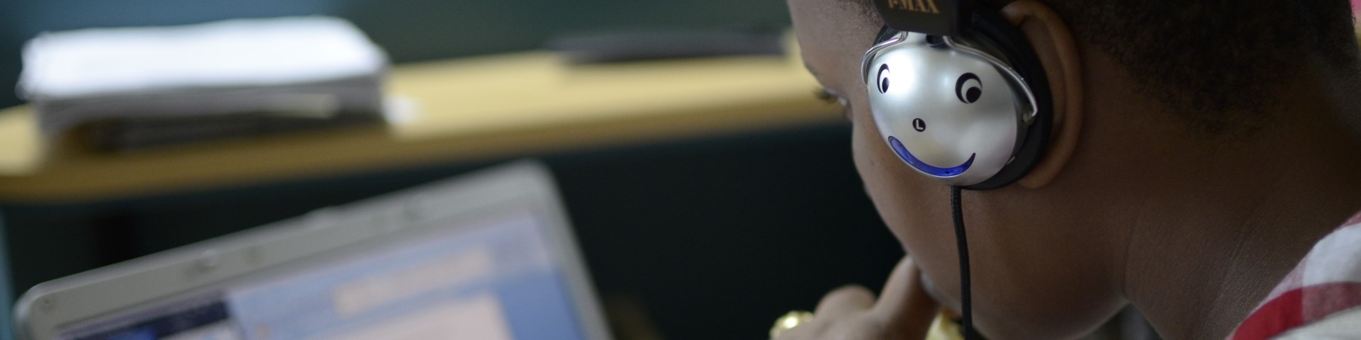 A boy wearing headphones sits in front of a laptop.