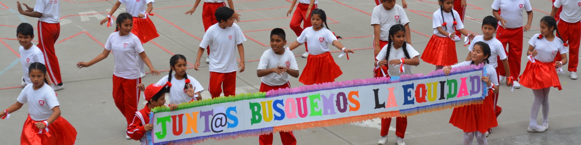 Children dance in a school playground. They hold a sign that reads ‘Juntas busquemos la equidad’.