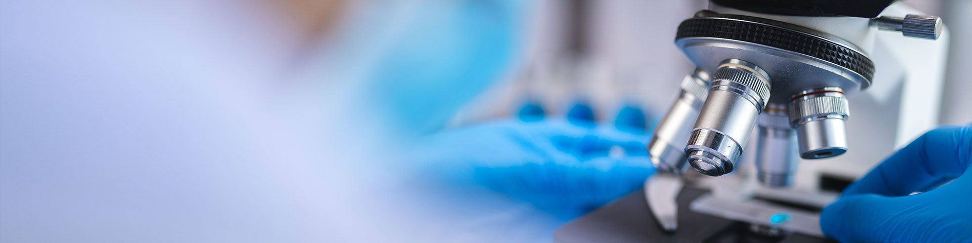 A person in blue gloves adjusts a microscope, representing the improvement of forensic skills to combat gender-based violence in Côte d'Ivoire.