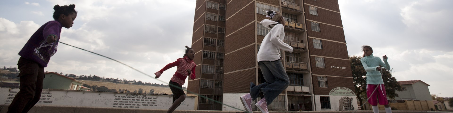 Children playing jump rope in front of a high-rise building, illustrating community life and activities.